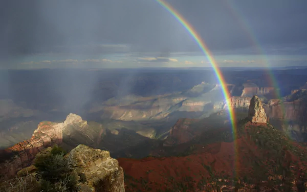 4K Ultra HD desktop wallpaper featuring a vibrant rainbow arching over a vast canyon landscape under a cloudy sky, highlighting nature's beauty.