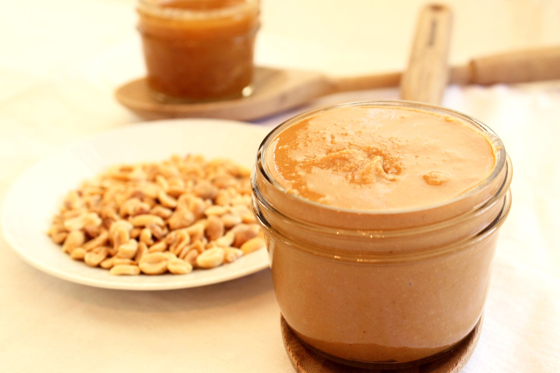 A close-up view of creamy peanut butter in a jar, surrounded by peanuts on a plate, creating a warm, inviting food-themed HD desktop wallpaper.