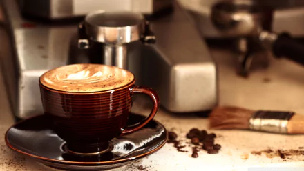 A close-up of a cappuccino in a striped cup, resting on a black saucer. The background features coffee beans and an espresso machine, creating a warm, inviting atmosphere.