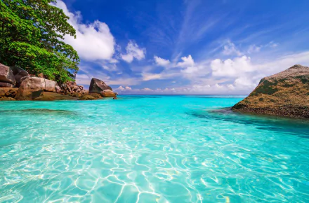 HD desktop wallpaper showcasing a tropical lagoon with clear turquoise sea, bright sky, lush greenery, and large rocks under a vibrant blue sky.