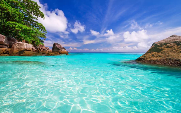 HD desktop wallpaper showcasing a tropical lagoon with clear turquoise sea, bright sky, lush greenery, and large rocks under a vibrant blue sky.