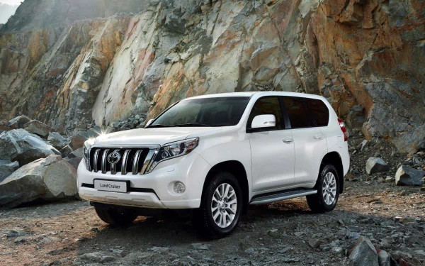 A Toyota Land Cruiser Prado parked on rocky terrain, showcasing its rugged design and capabilities, with a backdrop of natural rock formations.