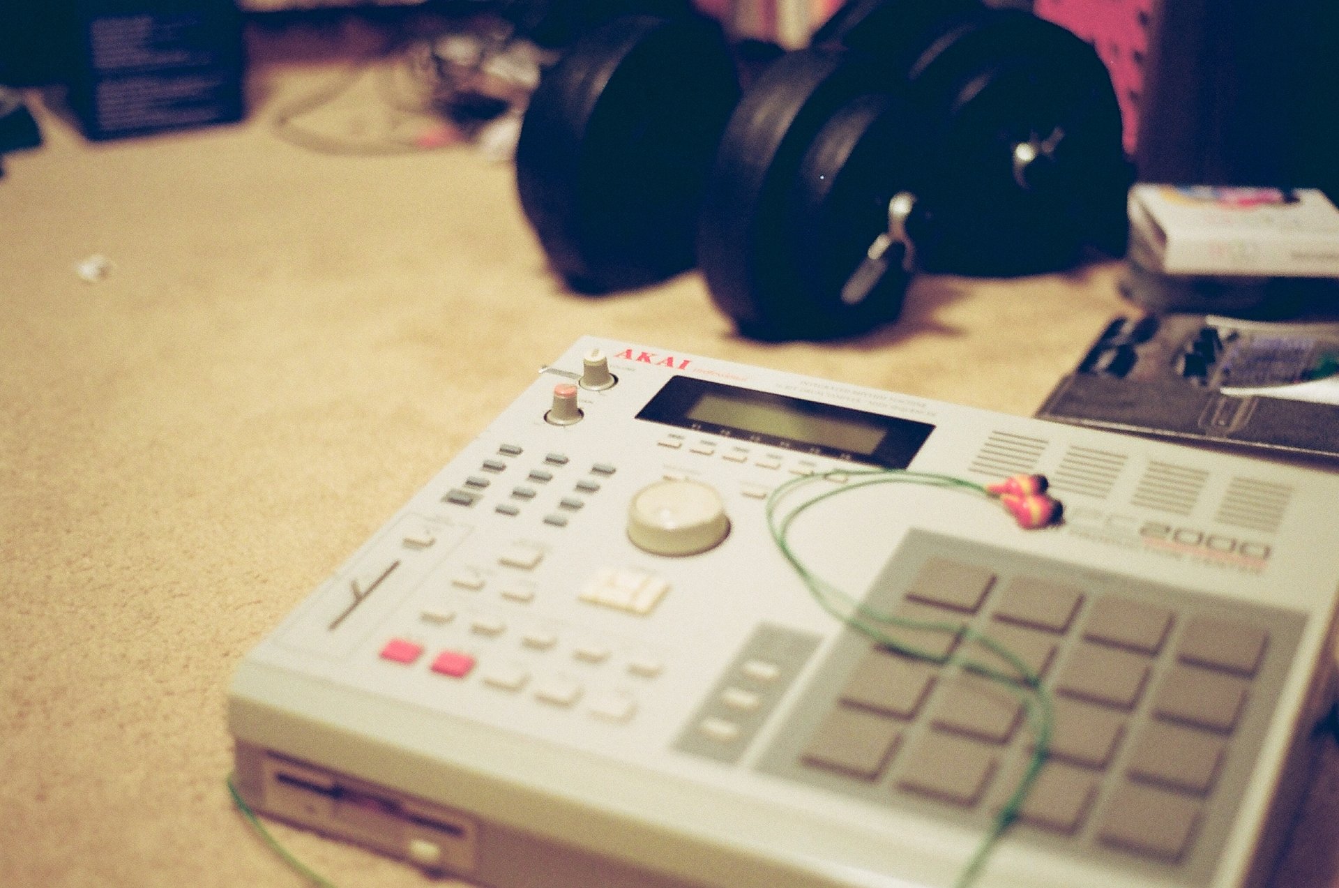 HD desktop wallpaper featuring a close-up of a music sampler with headphones on a carpeted floor, giving off a creative, casual vibe.