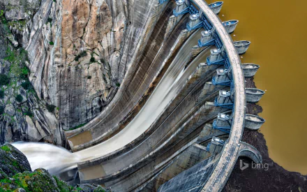 Aerial view of a man-made dam showcasing cascading water and intricate engineering against a backdrop of rugged rock formations. High-definition desktop wallpaper and background.