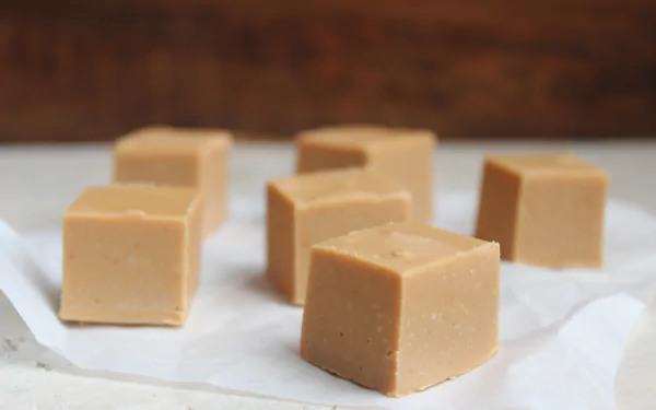 Close-up of smooth peanut butter fudge cubes on parchment paper, captured in 4K Ultra HD for a rich and detailed food desktop wallpaper.