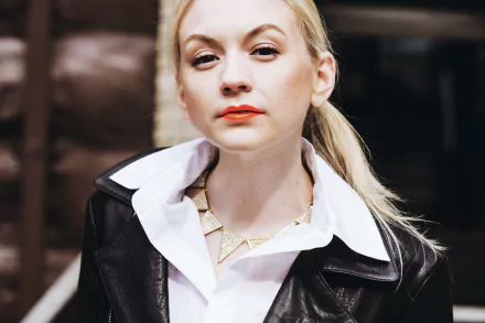 HD desktop wallpaper of celebrity Emily Kinney wearing a black leather jacket and white collared shirt, with a confident expression against a blurred background.