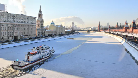 A motorship navigates the frozen Moscow River, surrounded by iconic architecture of Moscow, Russia, showcasing the blend of man-made beauty in a winter landscape.