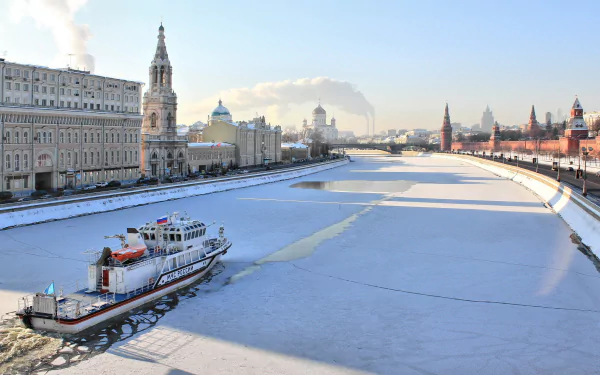 A motorship navigates the frozen Moscow River, surrounded by iconic architecture of Moscow, Russia, showcasing the blend of man-made beauty in a winter landscape.