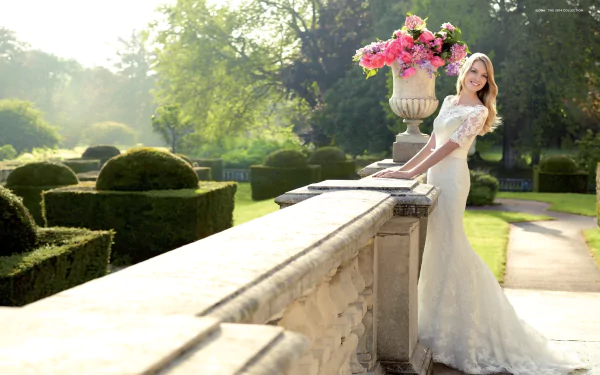 HD desktop wallpaper featuring Lindsay Ellingson in a white dress, standing by a stone railing with vibrant flowers and manicured garden greenery in the background.