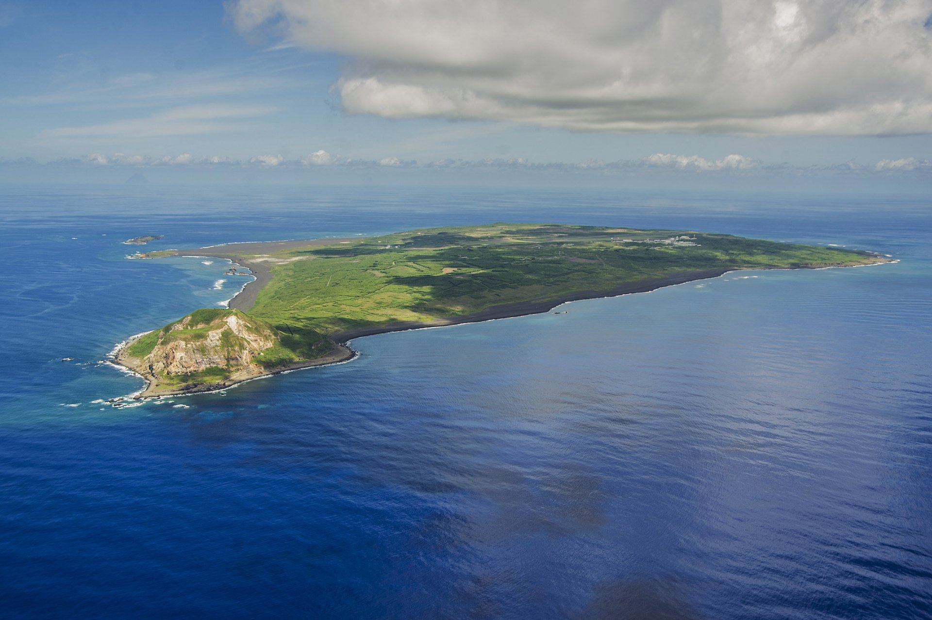 Aerial view of Iwo Jima island surrounded by ocean water under cloudy skies, showcasing natural beauty near Tokyo, Japan.