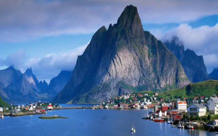 2K Quad HD PC desktop wallpaper: photography of Reine, Lofoten, Norway — a steep mountain rising above a fjord with a colorful coastal village and calm blue sky.