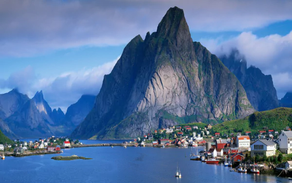2K Quad HD PC desktop wallpaper: photography of Reine, Lofoten, Norway — a steep mountain rising above a fjord with a colorful coastal village and calm blue sky.