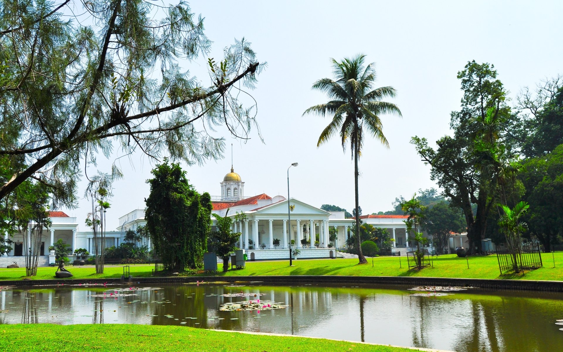 Bogor Palace, a man-made white colonial estate beside a reflective pond and palm trees, presented as a 2K Quad HD PC desktop wallpaper and background.