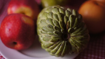 HD PC desktop wallpaper showing a close-up green sugar apple (custard apple) on a plate with red and orange apples as a food background