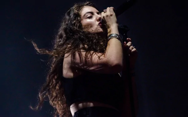 Moody close-up of a female singer mid-performance with long dark hair and mic, deep stage shadows. 5K Ultra HD PC desktop wallpaper/background. Tags: music, Lorde.