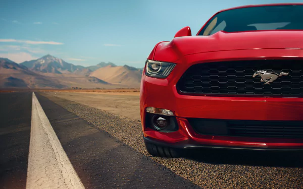 A high-definition desktop wallpaper featuring the front view of a red 2015 Ford Mustang GT on a deserted road with mountains in the background.
