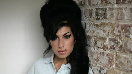 Portrait of an English female singer with a beehive hairstyle and winged eyeliner against a brick wall — music-themed 2K Quad HD PC desktop wallpaper.
