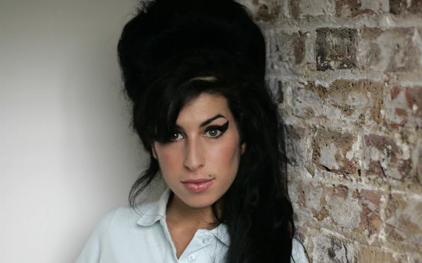 Portrait of an English female singer with a beehive hairstyle and winged eyeliner against a brick wall — music-themed 2K Quad HD PC desktop wallpaper.