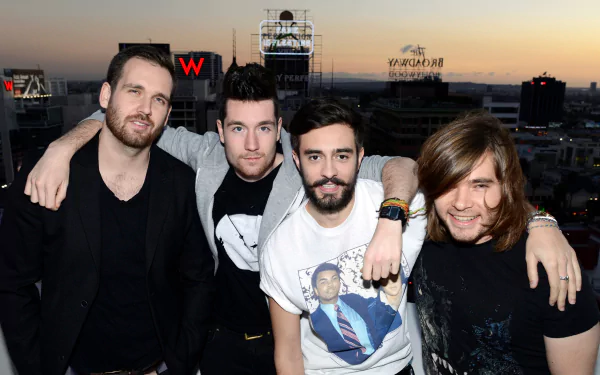 HD desktop wallpaper featuring the English rock band Bastille posing together against a city skyline at sunset.