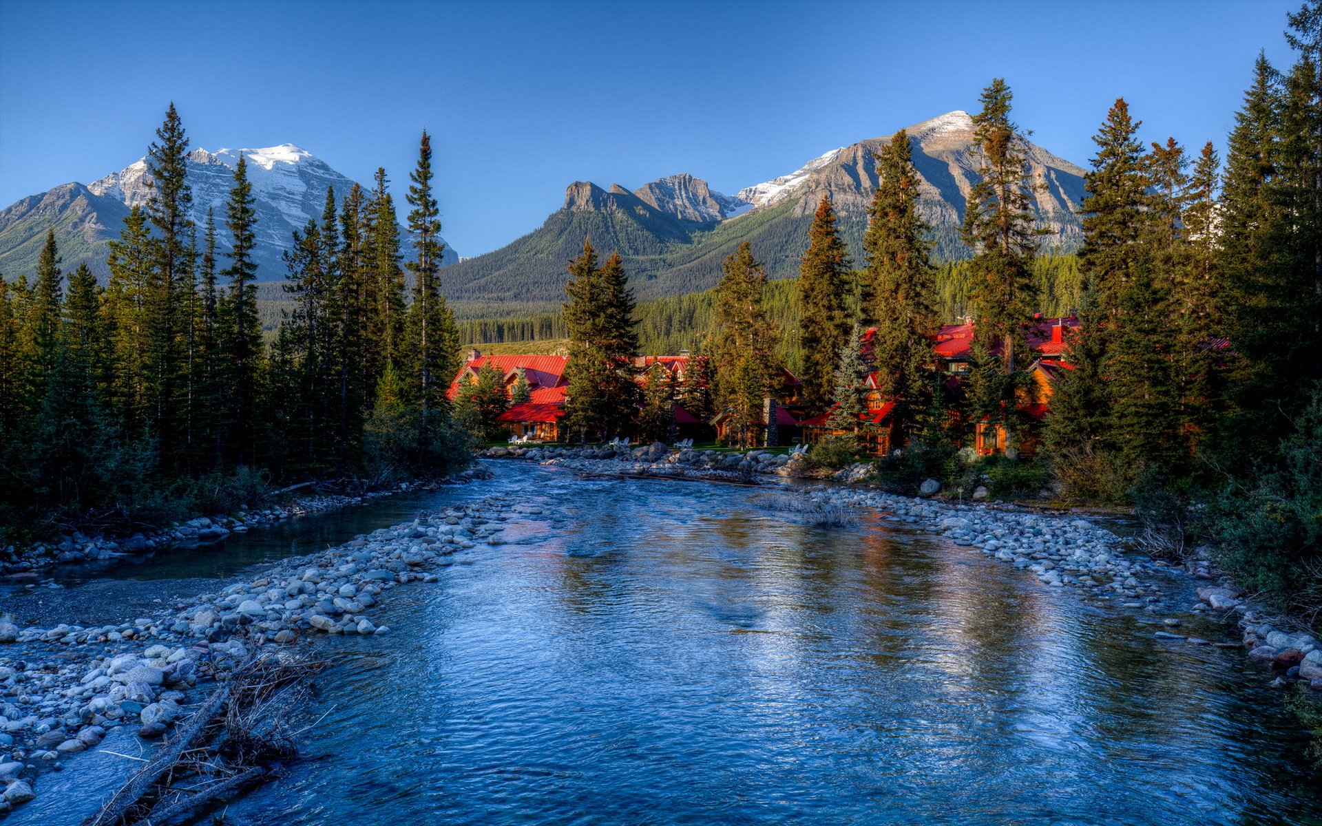 HD landscape photography of a serene river flowing through a forest with snow-capped mountains in the background, featured as a PC desktop wallpaper and background.
