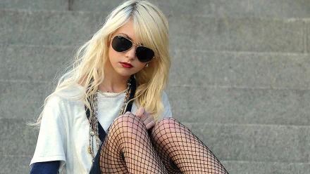 HD desktop wallpaper featuring Taylor Momsen wearing dark sunglasses, fishnet stockings, and layered clothing, set against a gray stone background.