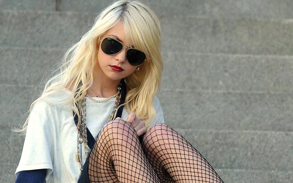 HD desktop wallpaper featuring Taylor Momsen wearing dark sunglasses, fishnet stockings, and layered clothing, set against a gray stone background.