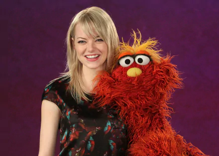 HD desktop wallpaper featuring celebrity Emma Stone smiling alongside a bright orange Muppet character against a purple background.