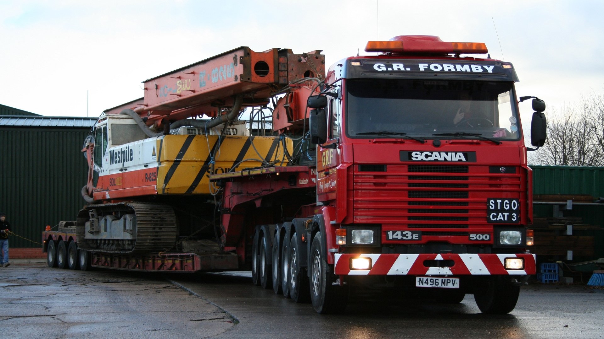 HD desktop wallpaper featuring a red Scania truck transporting heavy construction equipment on a trailer.