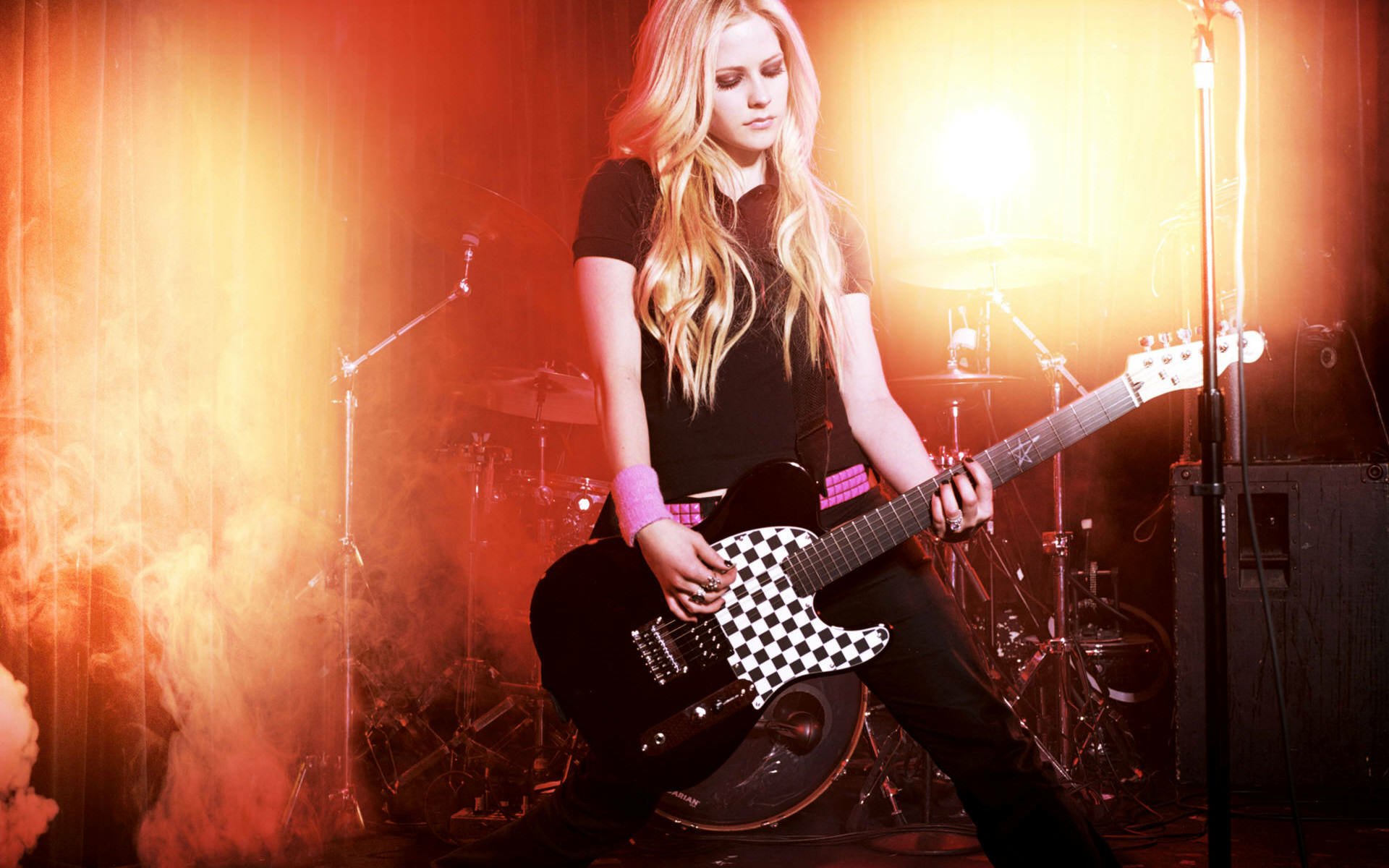 HD PC desktop wallpaper featuring Avril Lavigne playing a guitar on stage, bathed in warm orange and yellow concert lighting, highlighting her music performance.