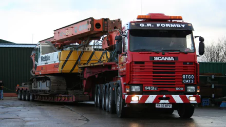 HD desktop wallpaper featuring a red Scania truck transporting heavy construction equipment on a trailer.