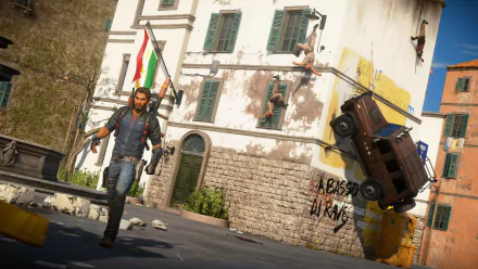 Rico Rodriguez from Just Cause 3 strides confidently through a chaotic scene, featuring a flying car and graffiti on a weathered building, showcasing the game's dynamic action.