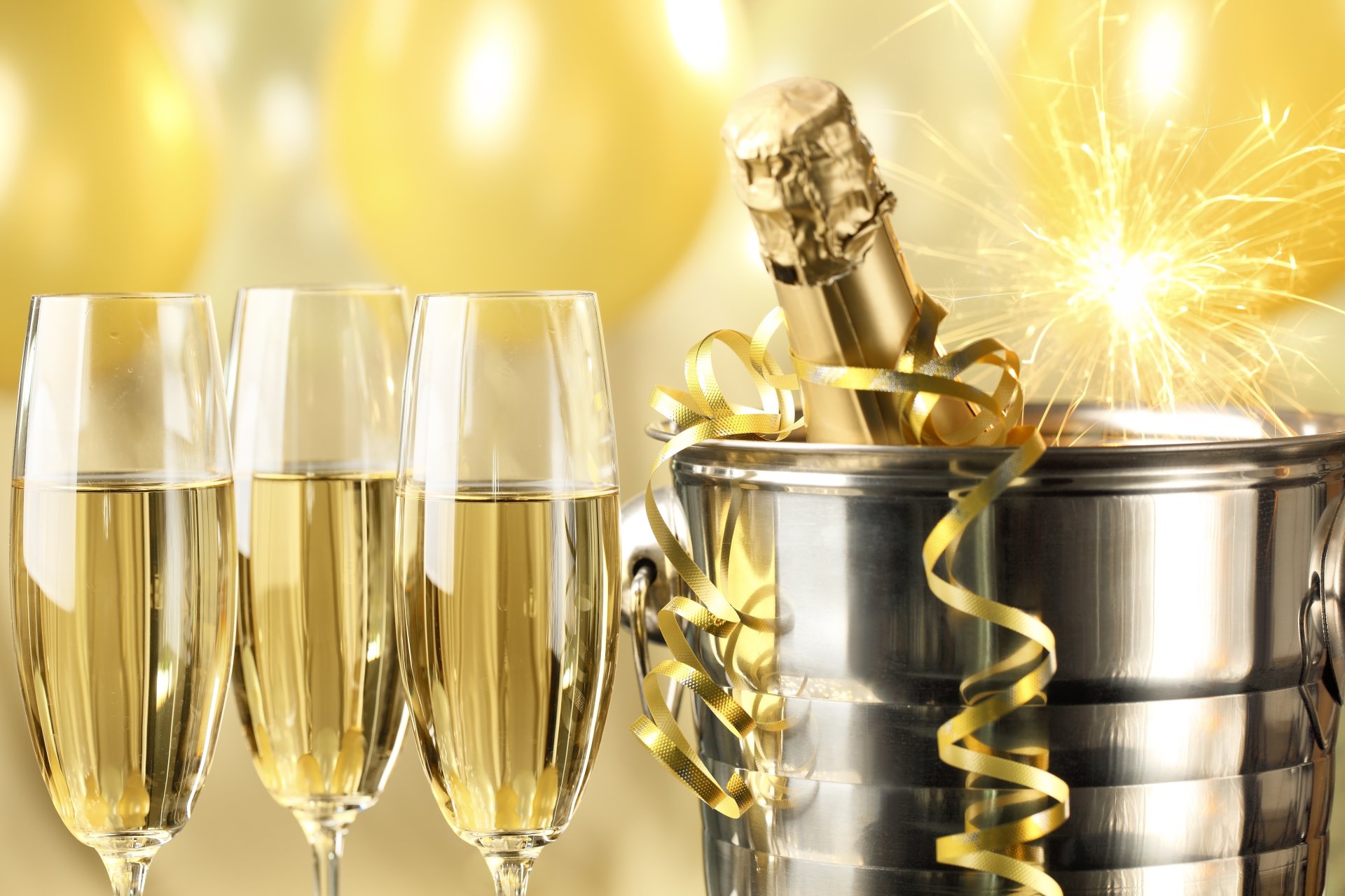Holiday New Year 5K Ultra HD PC desktop wallpaper and background: three champagne flutes, a champagne bottle in an ice bucket with gold ribbons, a lit sparkler and golden balloons.