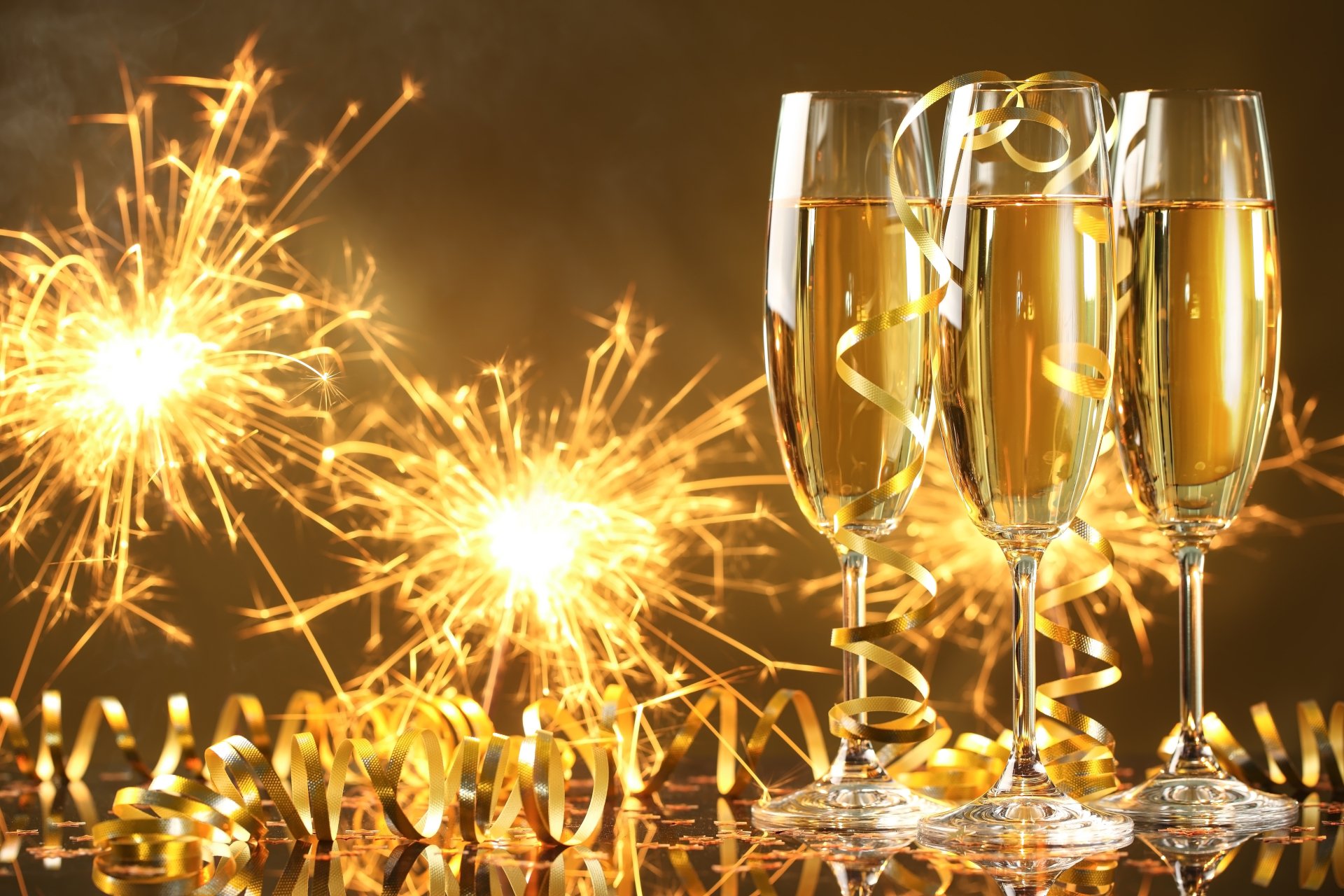 4K Ultra HD desktop wallpaper featuring three champagne glasses and sparkling holiday sparklers celebrating the New Year with golden tones and festive glow.