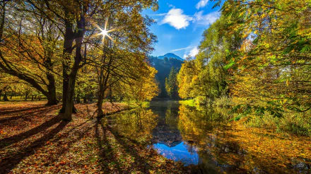 HD desktop wallpaper featuring a serene autumn landscape in Tyrol, Austria, with vibrant fall foliage, a reflective pond, trees, and a sunlit sky.