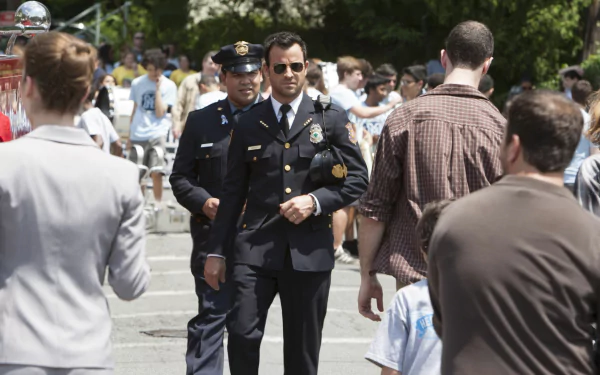 HD desktop wallpaper from the TV show The Leftovers featuring a police officer walking through a crowded outdoor scene with people engaged in various activities.