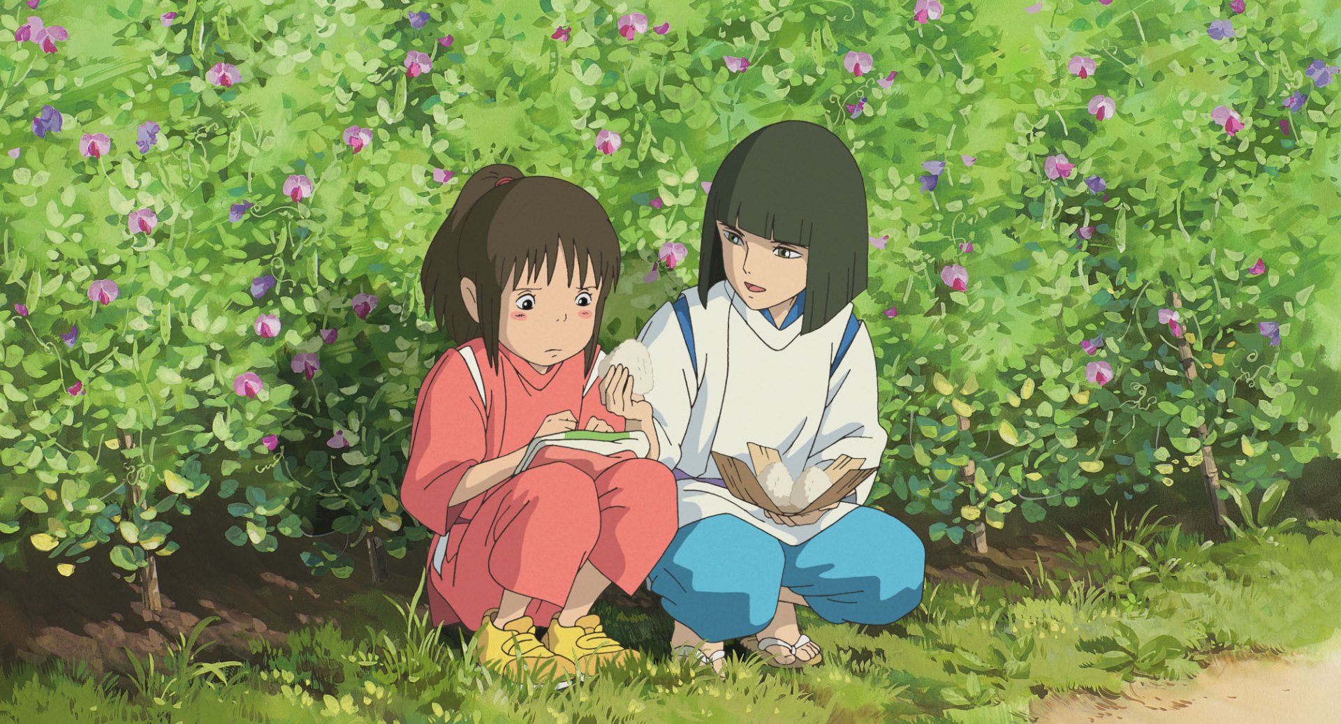 Two young girls from the anime Spirited Away sit in a vibrant green garden filled with flowers, engaged in a quiet moment together. A serene HD PC desktop wallpaper capturing their bond.