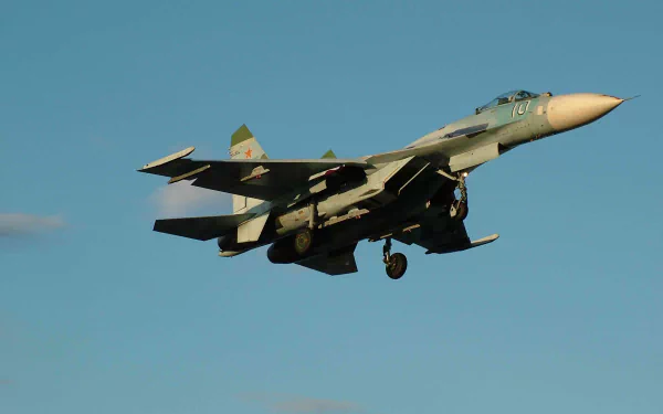HD desktop wallpaper of a military jet fighter, the Sukhoi Su-27, captured mid-flight against a clear blue sky.