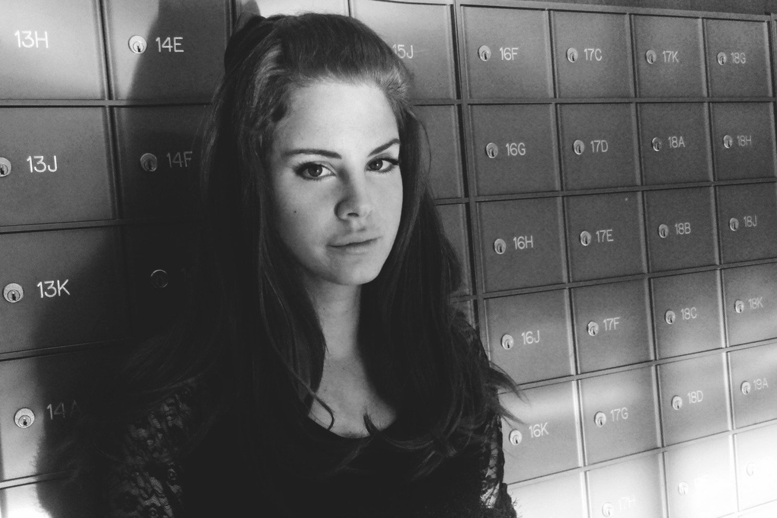 Black and white HD desktop wallpaper featuring Lana Del Rey standing against a wall of numbered lockers, capturing a moody and vintage music vibe.