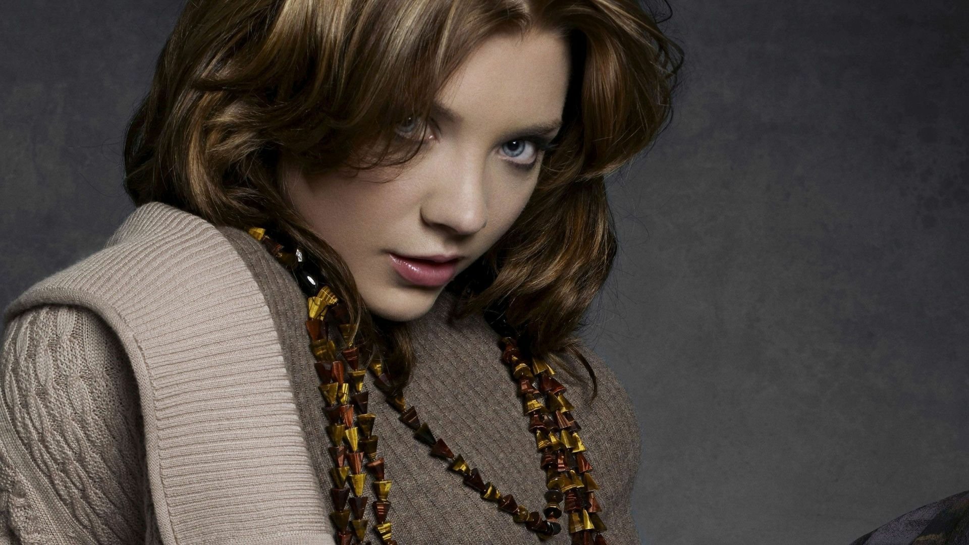 HD PC desktop wallpaper featuring celebrity Natalie Dormer with a contemplative expression, styled hair, and layered clothing against a dark background.