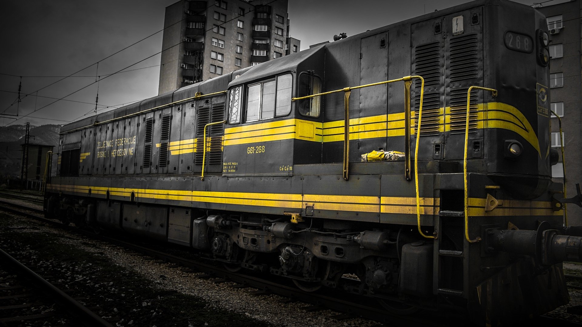 HD PC desktop wallpaper featuring a vintage train with yellow stripes, set against urban buildings in a dramatic black-and-white style.