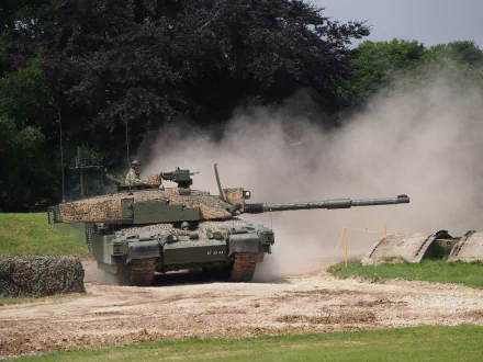 4K Ultra HD image of a Challenger 2 military tank advancing on a dirt path, kicking up dust against a backdrop of trees.