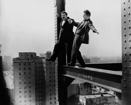 Black-and-white 4K Ultra HD PC desktop wallpaper of two men in classic comic-duo attire teetering on a steel beam high above a city skyline.