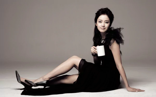 Kim Tae-hee, Korean celebrity, sits gracefully in a black dress holding a white mug, smiling against a neutral background in this HD PC desktop wallpaper.