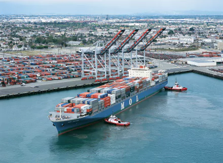 A large container ship, loaded with colorful shipping containers, maneuvers in the harbor, surrounded by cranes and a bustling port backdrop. A striking HD wallpaper option.