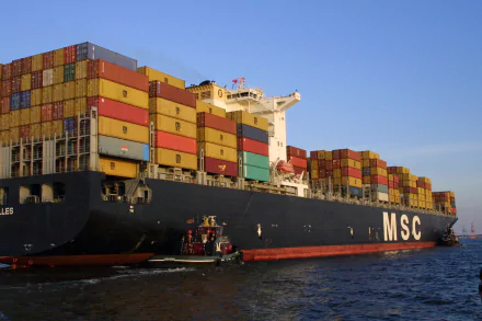 A large container ship loaded with colorful shipping containers navigates the water, showcasing maritime logistics in a striking HD desktop wallpaper.