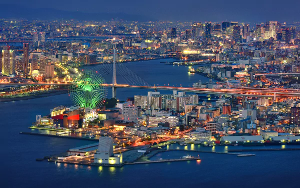 A stunning HD cityscape of Osaka, Japan, featuring illuminated buildings and a vibrant ferris wheel, showcasing the dynamic man-made environment at dusk.