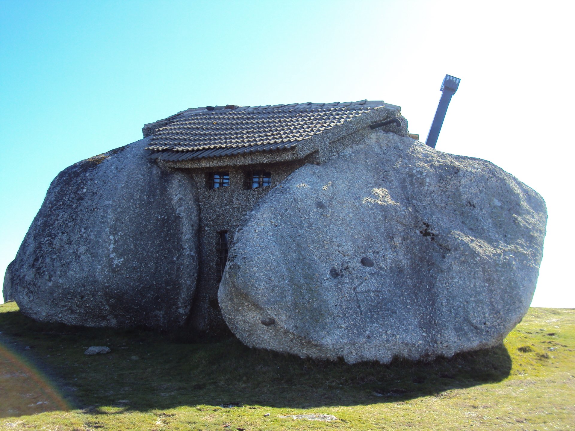 A unique man-made house built between two large boulders, shown in clear daylight as an HD PC desktop wallpaper and background.