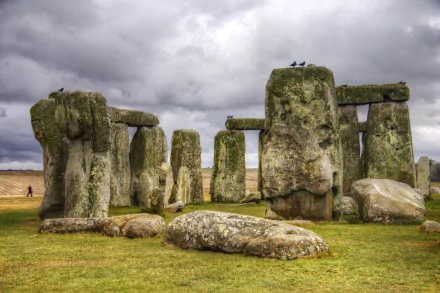 A stunning HD wallpaper of Stonehenge, showcasing its iconic stone structure under a cloudy sky, surrounded by lush green grass and a hint of rural landscape.