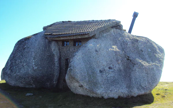 A unique man-made house built between two large boulders, shown in clear daylight as an HD PC desktop wallpaper and background.