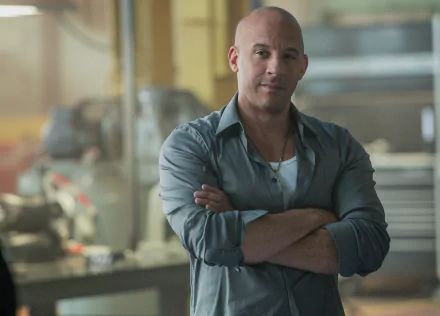 Vin Diesel as Dominic Toretto in a scene from Furious 7, standing with arms crossed in a mechanic's workshop. HD desktop wallpaper and background.